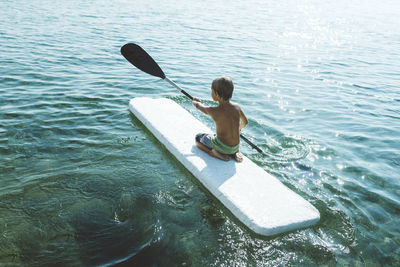 Rear view of shirtless boy paddleboarding on lake