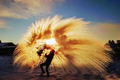 Man by splashing water at beach against sky during sunset