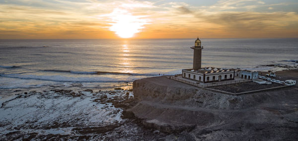 Lighthouse by sea against sky during sunset