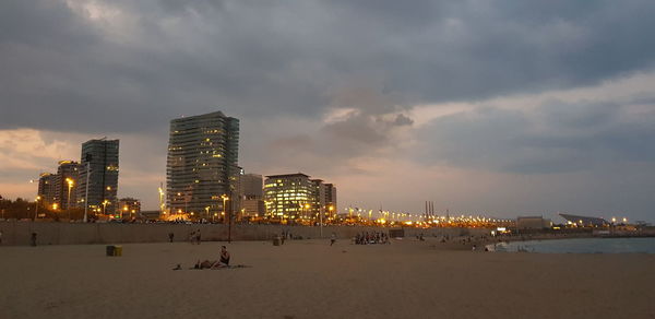 Illuminated buildings by sea against sky in city
