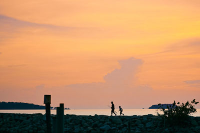 Silhouette people walking at beach against sky during sunset