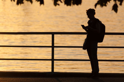 Silhouette woman using smart phone by railing against sea