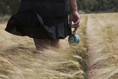 Midsection of woman holding alarm clock while standing amidst plants on land