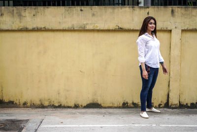 Portrait of young woman standing against wall