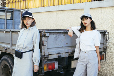 Portrait of friends standing by truck against wall in city