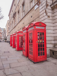 Red telephone booth on sidewalk by building in city