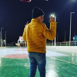 Rear view of man holding umbrella standing at night