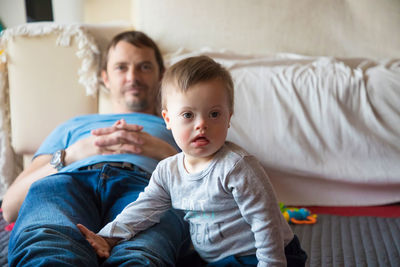 Portrait of father holding baby while sitting on sofa at home