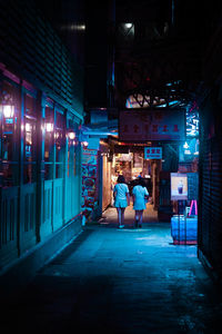 Rear view of people walking on illuminated street at night