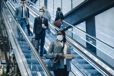 Male and female colleagues moving downwards on escalator during covid-19