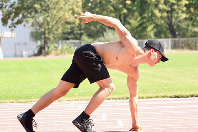 Side view of shirtless man running on track