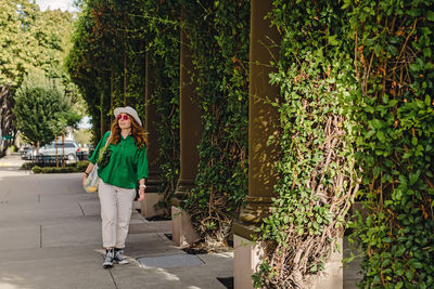 Young woman walking on the street holding a mesh bag with vegetables on her shoulder. 