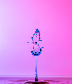Close-up of drop falling on water against pink background