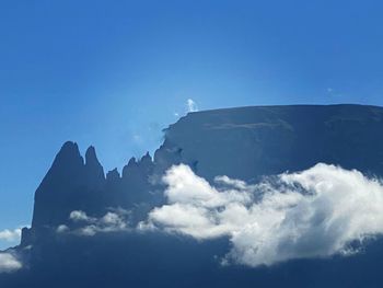 Low angle view of clouds over mountain against blue sky