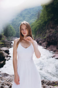 Portrait of young woman standing against river