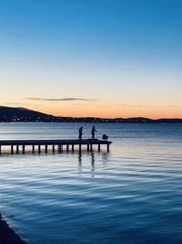 Silhouette people in sea against clear sky during sunset