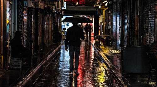 Rear view of man walking on wet road in city at night