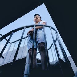 Low angle portrait of young man standing on steps against sky