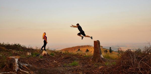 Woman with jumping man on field against sky during sunset