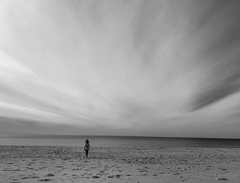Girl walking at beach against cloudy sky