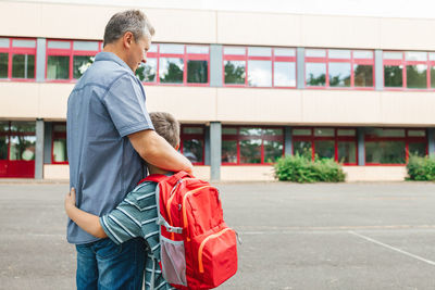 Happy dad hugs the child of the schoolboy and escorts him to school at the beginning of the lessons. 