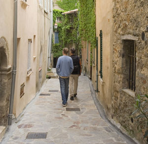 Rear view full length of friends walking on alley amidst buildings at ramatuelle