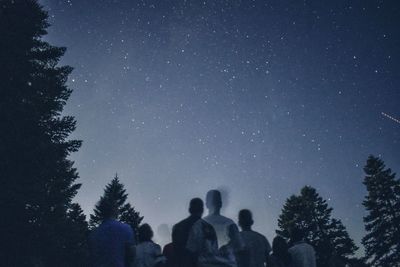 Digital composite image of people by trees against sky at night