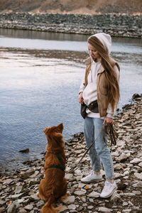 Young woman and dog retriever walks on river shore at autumn season