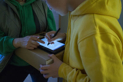 Boy signing on screen with digitized pen while receiving package