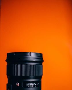 Close-up of camera lens against orange wall