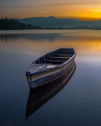 Boat moored on lake against sky during sunset