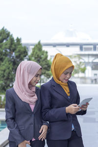 Businesswomen using digital tablet while standing on city street