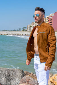 Young man wearing sunglasses standing by sea against sky