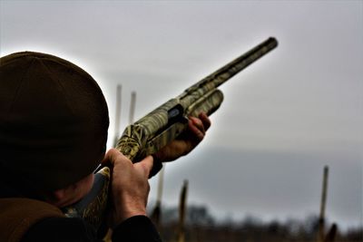 Close-up of man aiming rifle against sky