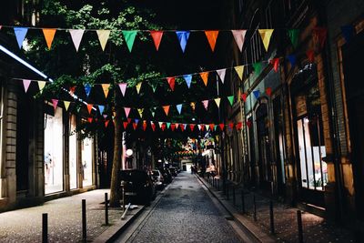 Illuminated lights hanging amidst buildings in city at night