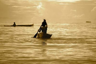 Silhouette men on boat in sea against sky