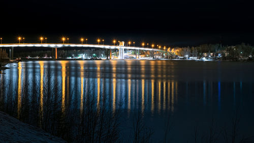 Illuminated bridge over river against sky at night