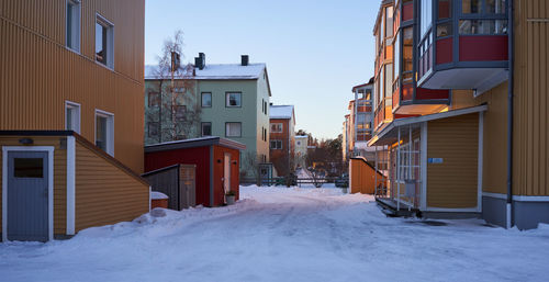 Snow covered street amidst houses and buildings in city