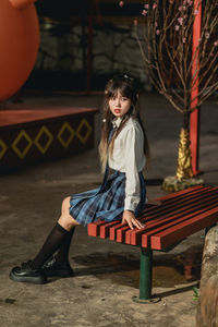 Portrait of young woman sitting on bench at park