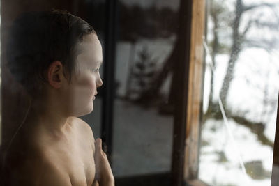 Thoughtful shirtless boy looking through window