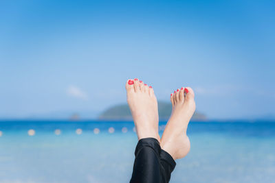 Low section of woman on beach against blue sky