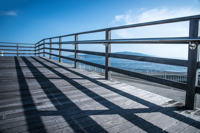 Shadow of railing on bridge over sea against sky