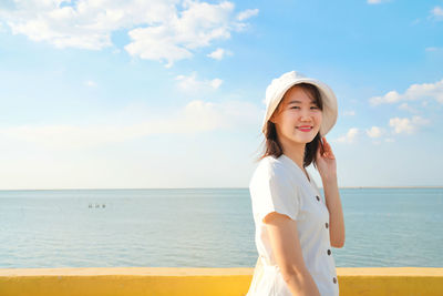 Portrait of smiling woman standing at beach against sky