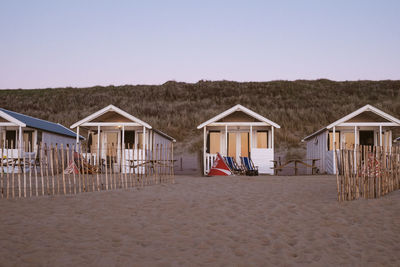 Hut on beach by houses against clear sky