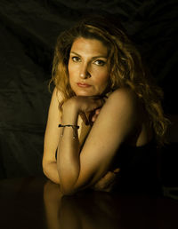 Portrait of woman sitting against black background