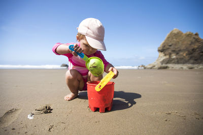 Young girl shovelling sand into bucket at the beach.