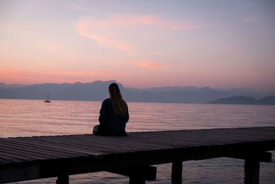 Silhouette woman sitting on pier over sea against sky during sunset