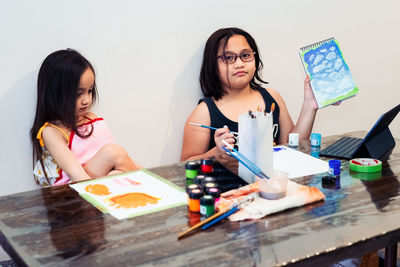 Cute little asian siblings painting a picture in home studio