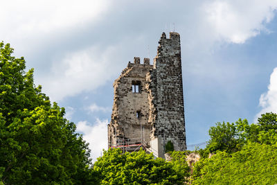 The ruins of a historical tower on a hill covered with trees in the background of blue sky
