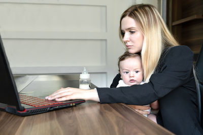 Young woman holds baby , in office, and working on laptop., concept of business and caring for baby